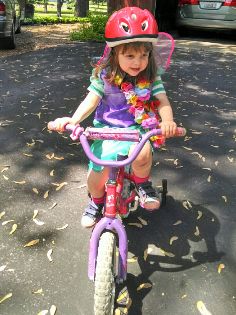 Lily with wings and lei riding her bike.