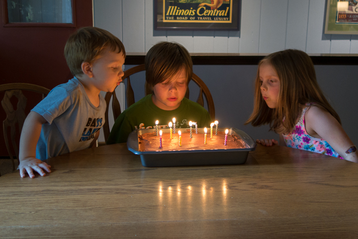 Jamie, Nate, and Lily blowing out birthday candles on Nate's birthday cake.